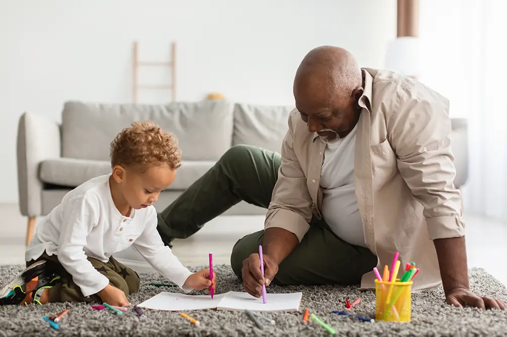 A grandpa and grandson sitting on the floor drawing together. A secure retirement investment.